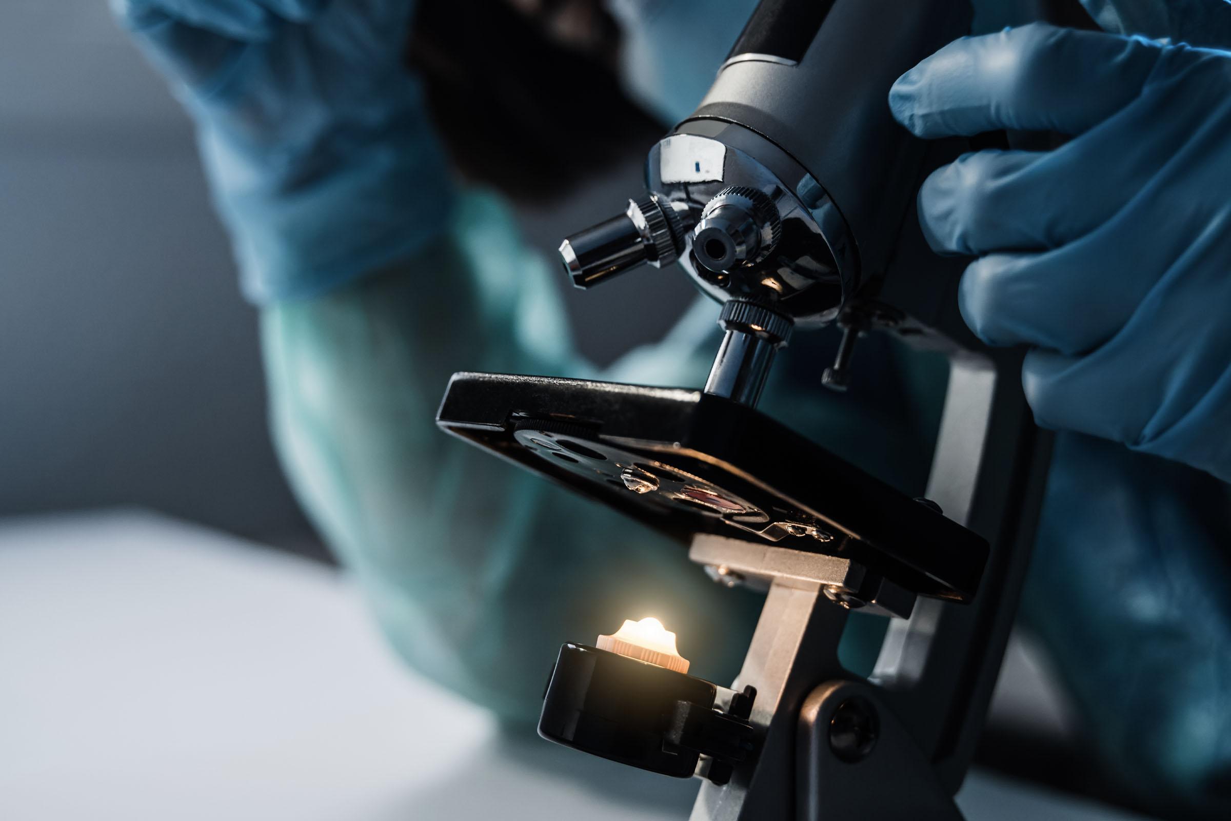 A microscope in focus with a person in personal protective equipment adjusting it