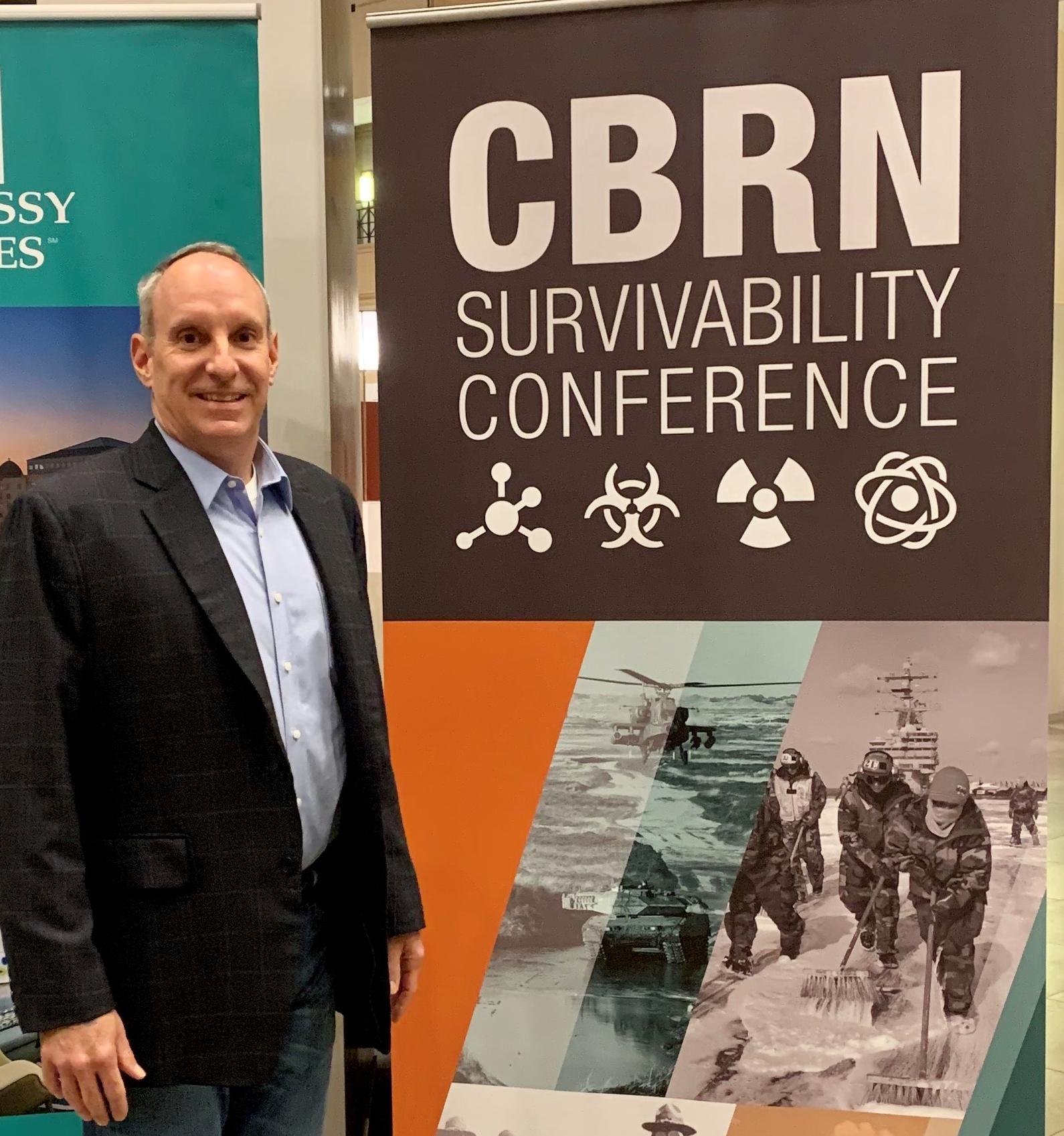 Ron Fizer in front of a banner for the CBRN Survivability Conference
